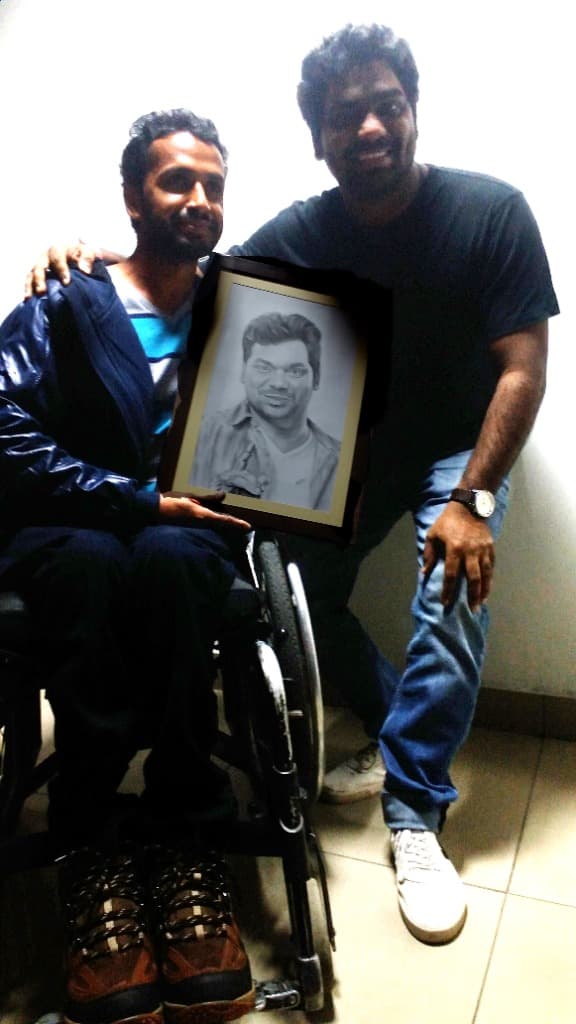 Imran in wheelchair holding a framed realistic pencil sketch portrait alongside a friend