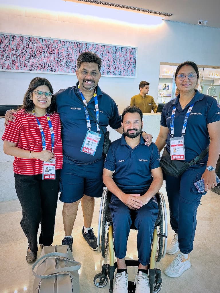 Mohammad Imran seated in wheelchair wearing Ottobock polo shirt with three fellow delegates and friends in event hall