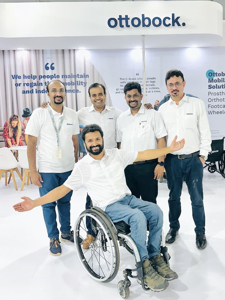 Mohammad Imran seated with arms outstretched in wheelchair with four smiling Ottobock team members in front of the Ottobock booth