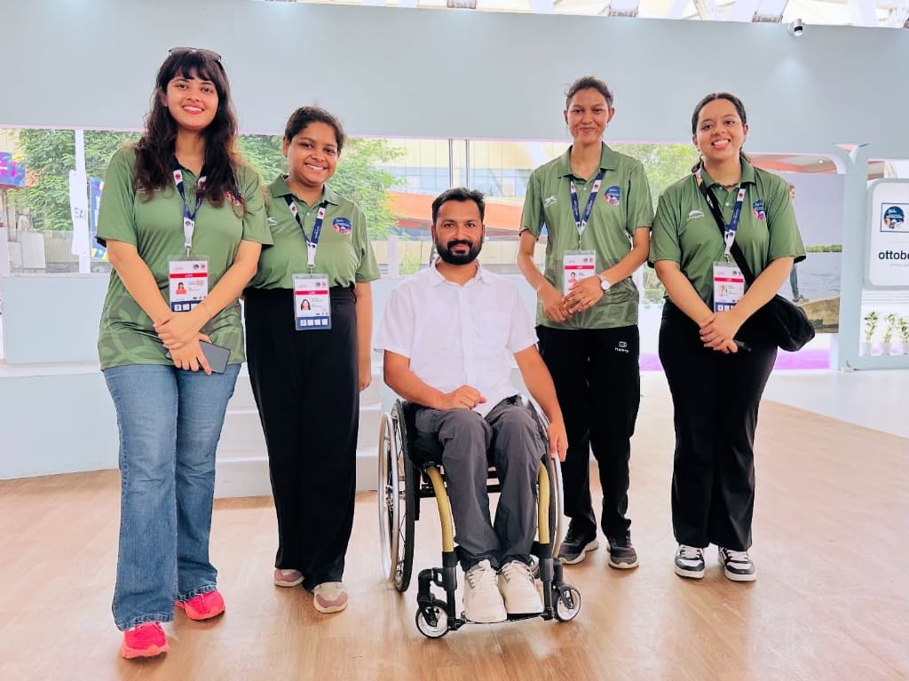Mohammad Imran in wheelchair surrounded by four smiling event coordinators and volunteers in green polo shirts